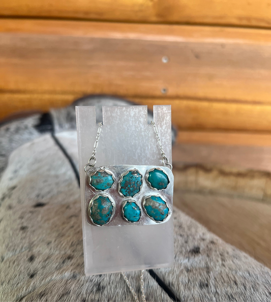 Hand Crafted Turquoise jewlery in a sterling silver necklace on a clear stand with a wooden background